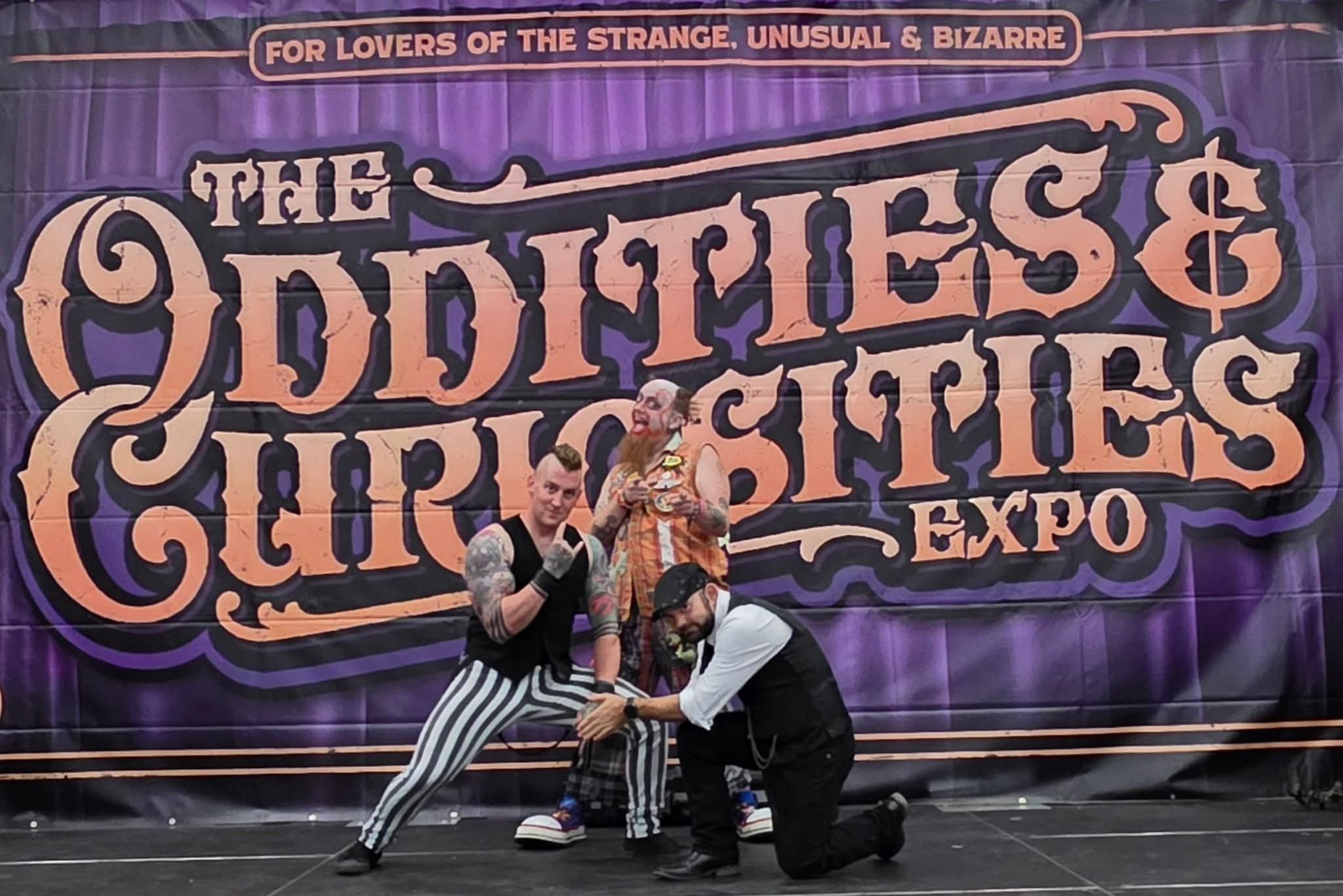 Reid Wilson performing at Oddities and Curiosities Expo with colorful sideshow backdrop and troupe members
