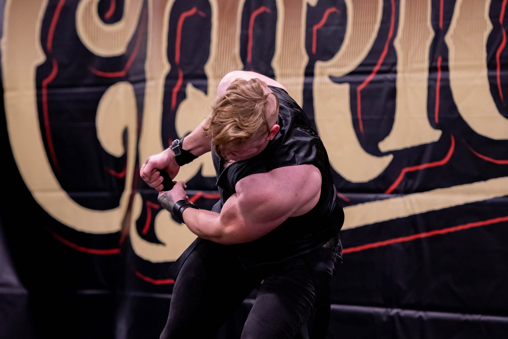 BF Reid performing intense steel bending act on stage with dramatic black and gold backdrop