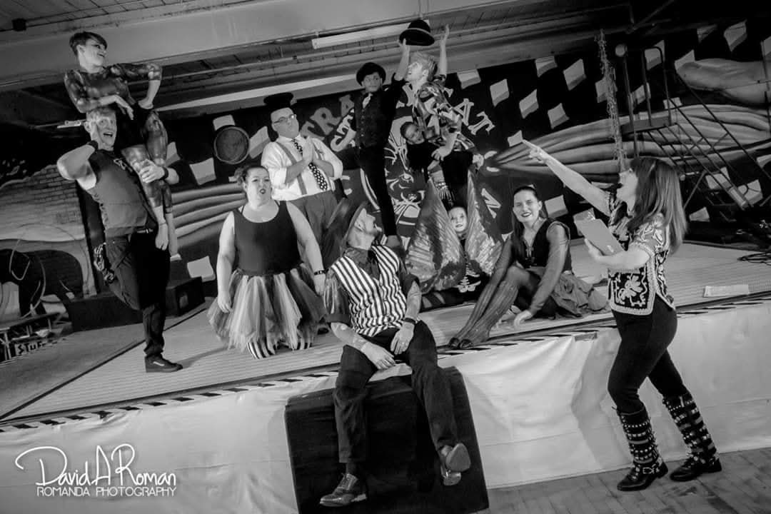 Black and white group photo of entire circus cast on stage with striped floor pattern and vintage props